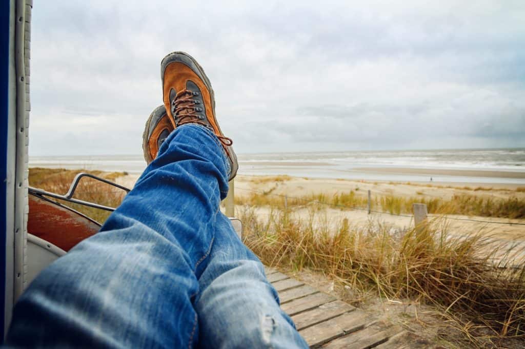 A person relaxing on the beach with their feet up as they look across the ocean towards the horizon.